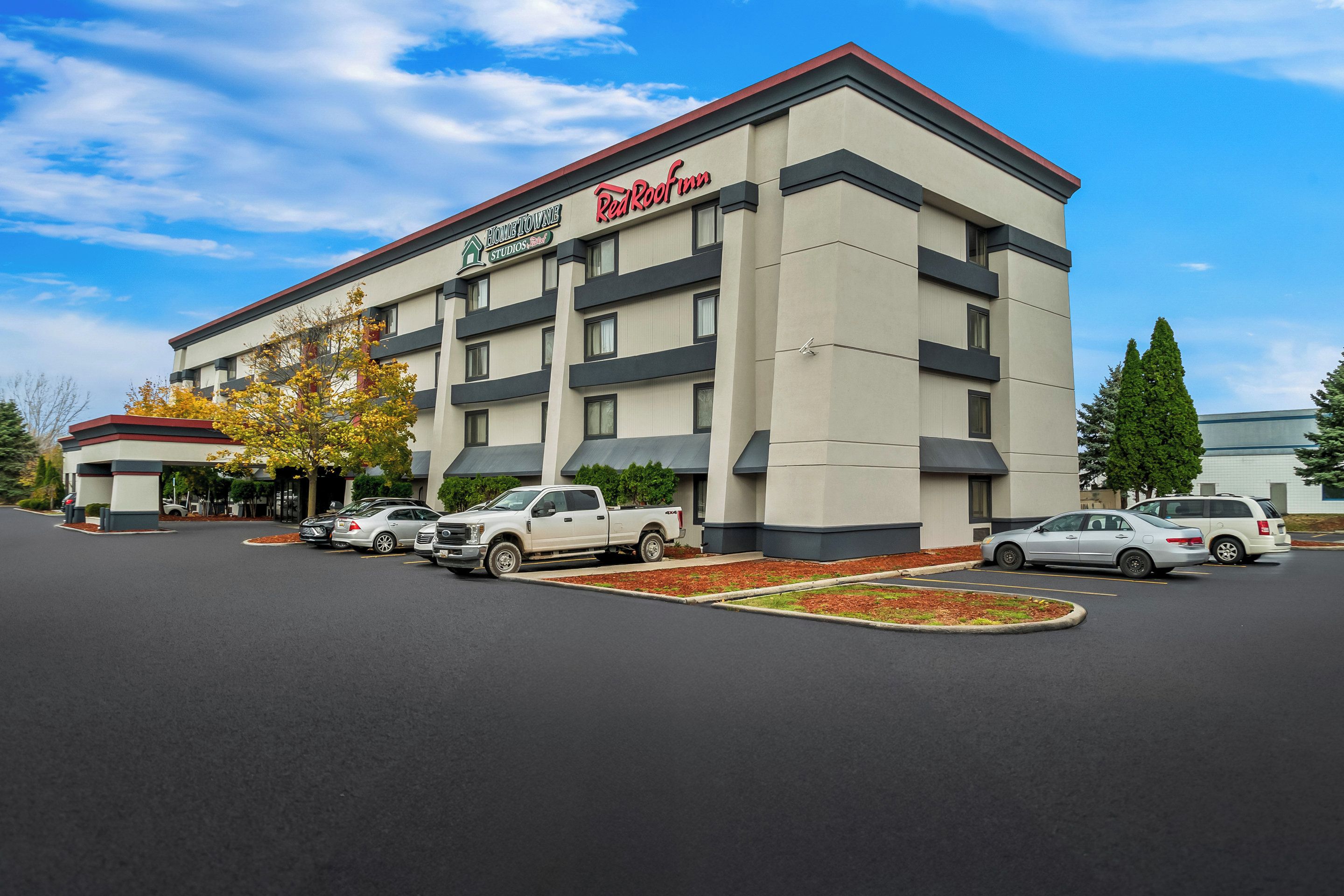 A hotel with a modern design, featuring a flat roof and a parking lot with several cars.