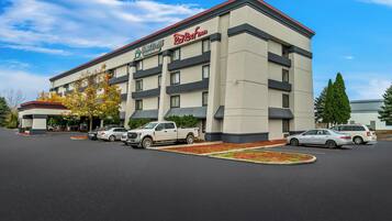 A hotel with a modern design, featuring a flat roof and a parking lot with several cars.