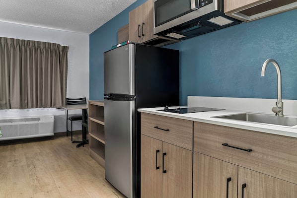 A modern kitchen with a built-in microwave, stainless steel refrigerator, and a sink with a faucet. - HomeTowne Studios by Red Roof Flint (Flint)
