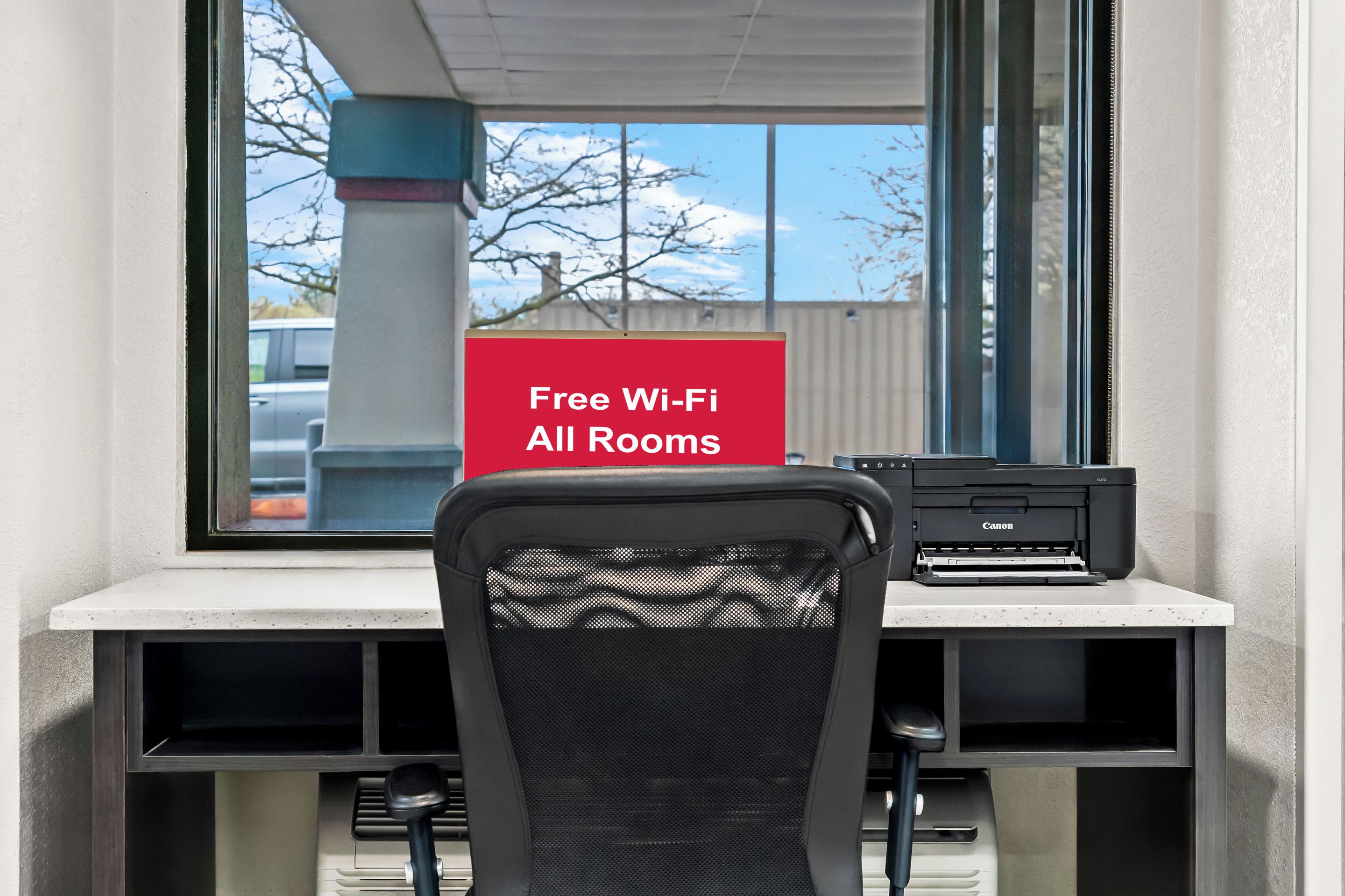 A workspace with a Canon printer, a black mesh chair, and a sign stating "Free Wi-Fi All Rooms".