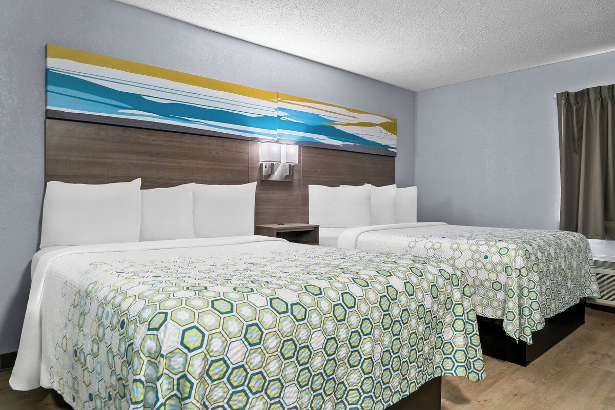 A hotel room with two beds, a large abstract painting on the wall, a nightstand, and a window with curtains.