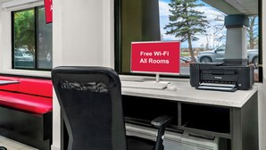 A workspace with a red sign indicating free Wi-Fi, a Canon printer, and a black office chair. - HomeTowne Studios by Red Roof Flint (Flint)