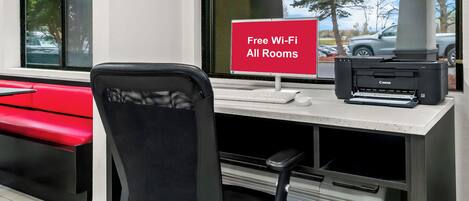 Un espacio de trabajo con un letrero rojo que indica Wi-Fi gratuito, una impresora Canon y una silla de oficina negra.