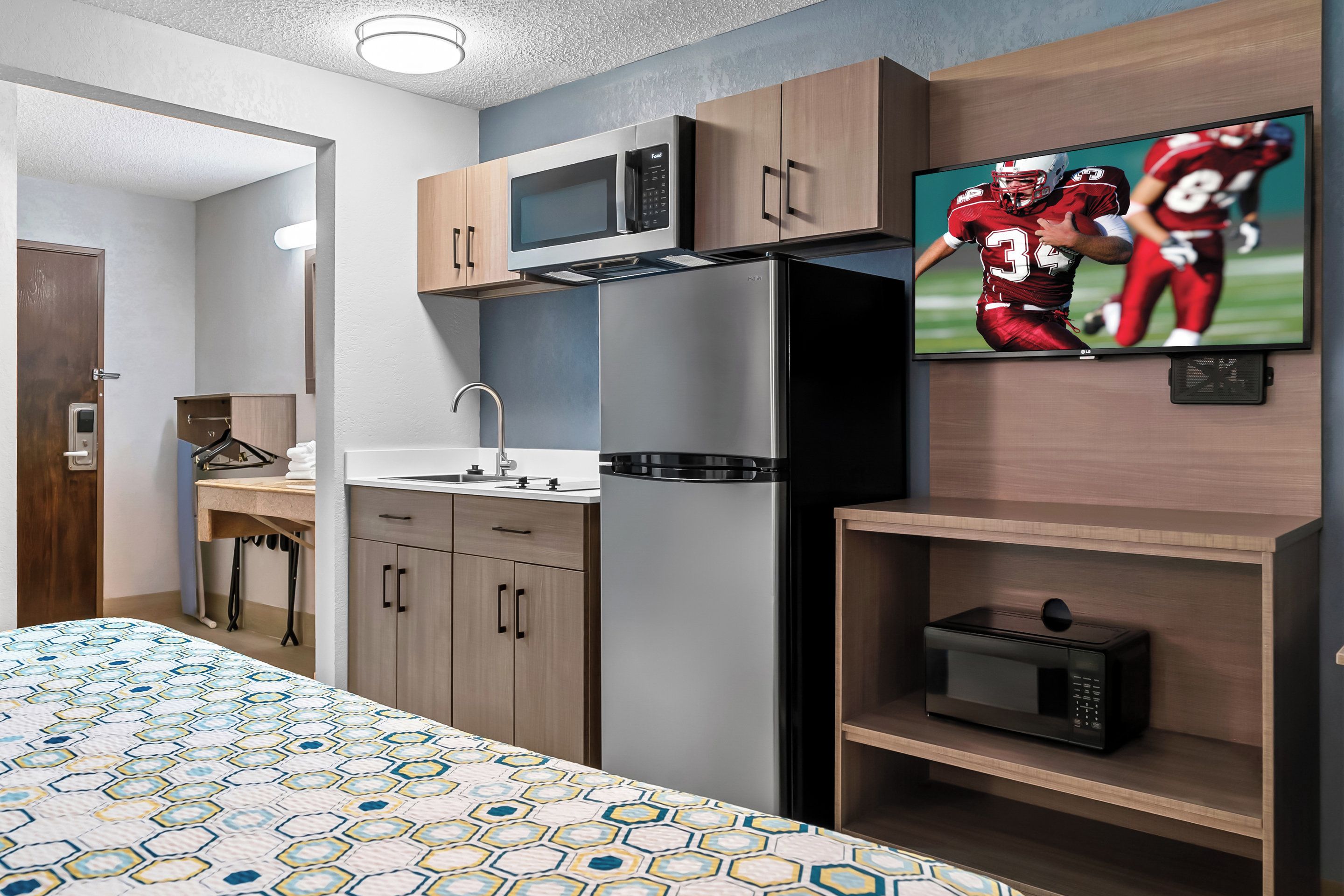 A compact hotel room with a bed, a microwave, a refrigerator, a TV, and a small shelf.
