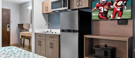 A compact hotel room with a bed, a microwave, a refrigerator, a TV, and a small shelf.