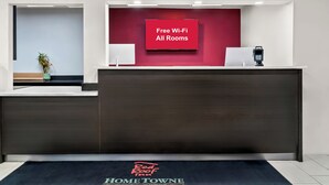 A hotel reception desk with a red wall and a sign stating "Free Wi-Fi All Rooms". - HomeTowne Studios by Red Roof Flint (Flint)