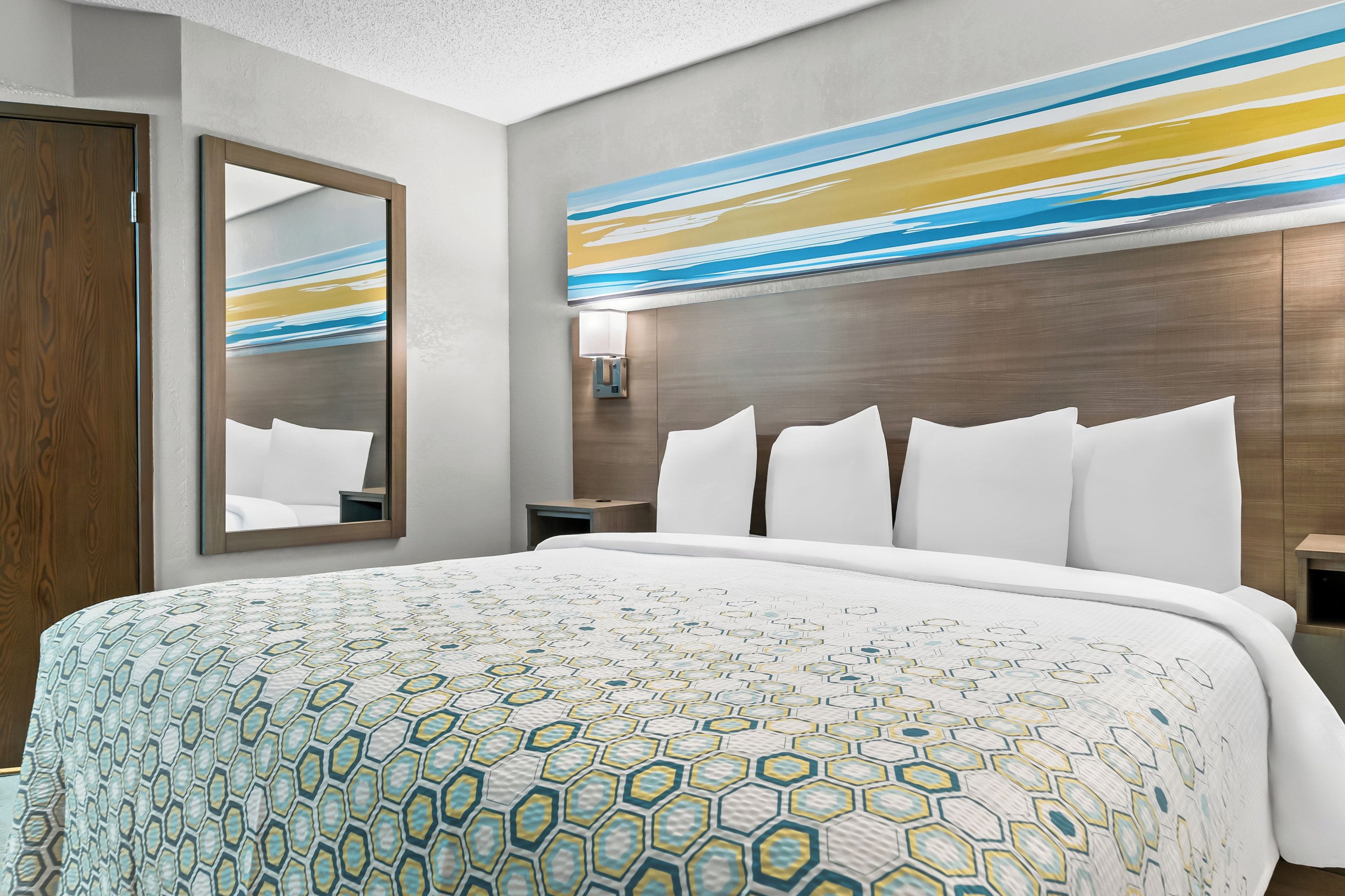 A hotel room with a large bed, a wooden wardrobe, a modern abstract painting, and a nightstand with a lamp.