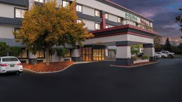 A hotel with a modern design, featuring a covered entrance and a parking area.