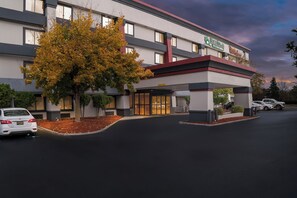 A hotel with a modern design, featuring a covered entrance and a parking area. - HomeTowne Studios by Red Roof Flint (Flint)