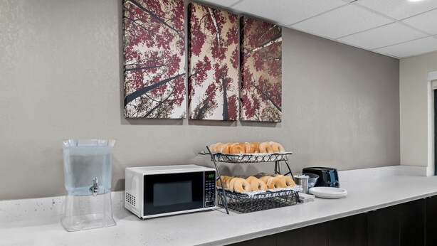 A breakfast bar with a water dispenser, a microwave, and a tray of pastries. - HomeTowne Studios by Red Roof Flint (Flint)