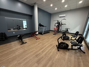 A gym with exercise equipment, a mirror, and a window. - HomeTowne Studios by Red Roof Flint (Flint)