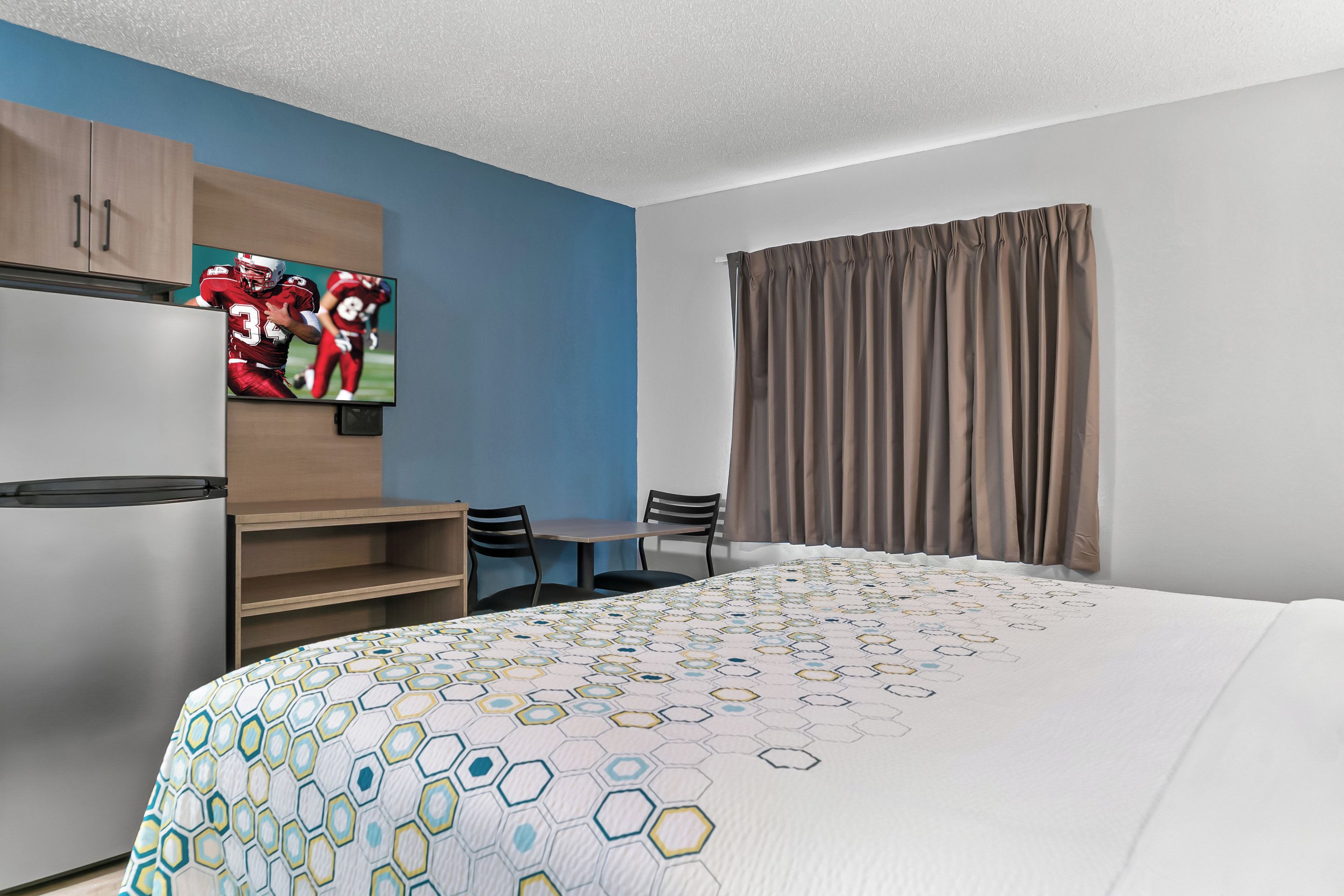 A hotel room with a large bed, a television on the wall, a desk with chairs, and a wardrobe.