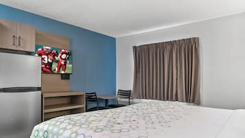 A hotel room with a large bed, a television on the wall, a desk with chairs, and a wardrobe.
