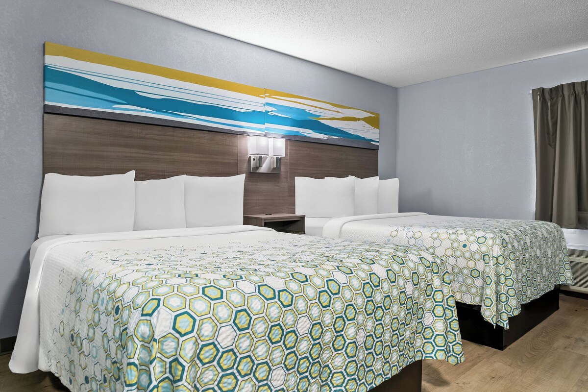 A hotel room with two beds, a large abstract painting on the wall, a nightstand, and a window with curtains.