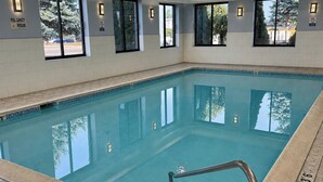 An indoor swimming pool with clear water, a tiled floor, and windows with a view of the outside. - HomeTowne Studios by Red Roof Flint (Flint)