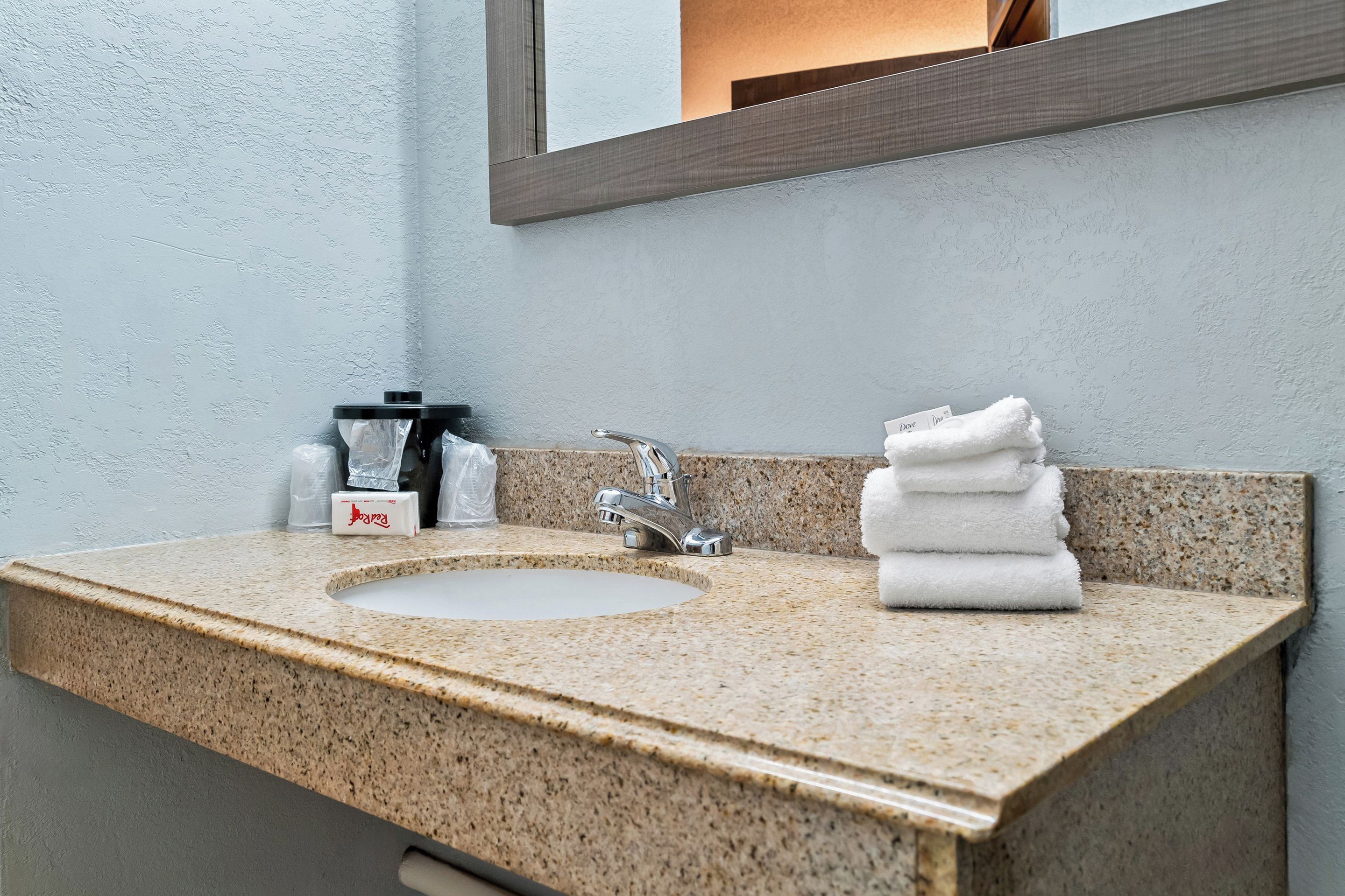 A bathroom with a granite countertop sink, a mirror, and a stack of white towels.
