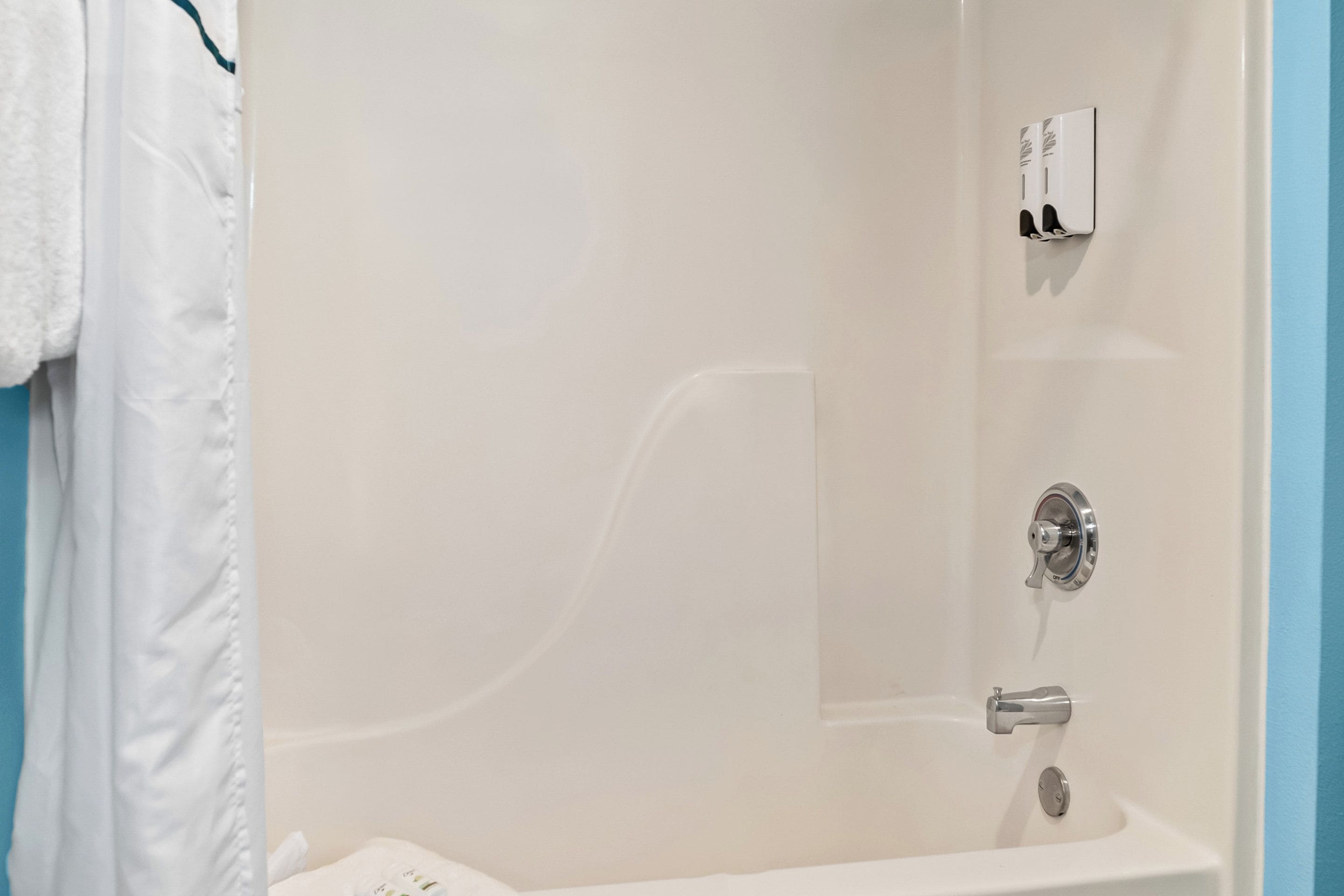 A bathroom with a bathtub, a towel rack, and a soap dispenser.