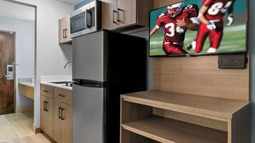 A modern kitchen with a built-in refrigerator, wooden cabinets, a microwave, and a flat-screen TV displaying a football game.