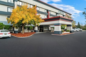 A hotel with a modern design, featuring a covered entrance and a parking area with several cars. - HomeTowne Studios by Red Roof Flint (Flint)
