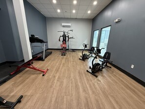 A gym with exercise equipment, a treadmill, and a stationary bike. - HomeTowne Studios by Red Roof Flint (Flint)