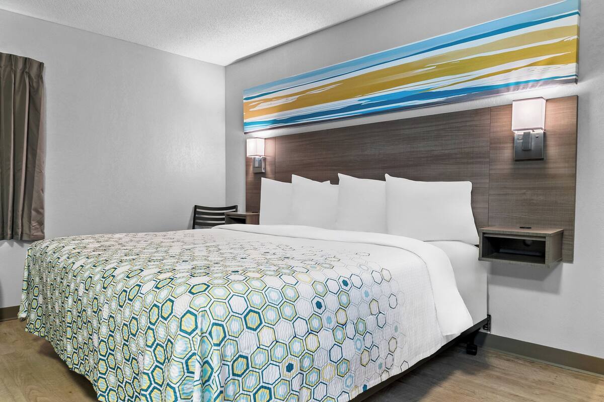A hotel room with a large bed, a headboard with a light fixture, a bedside table, and a wall-mounted light.