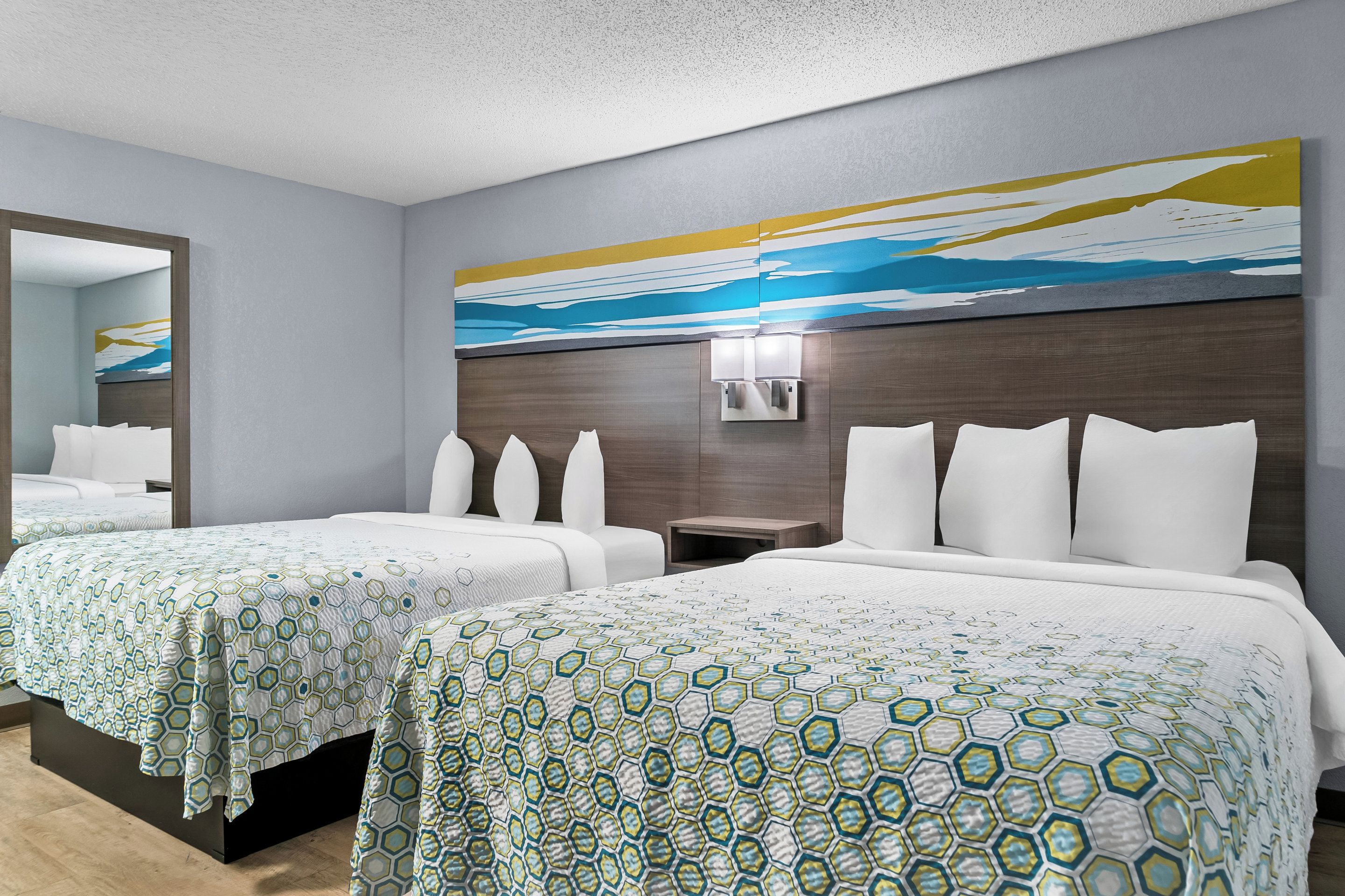 A hotel room with two beds, a large mirror, and a wall-mounted light fixture.