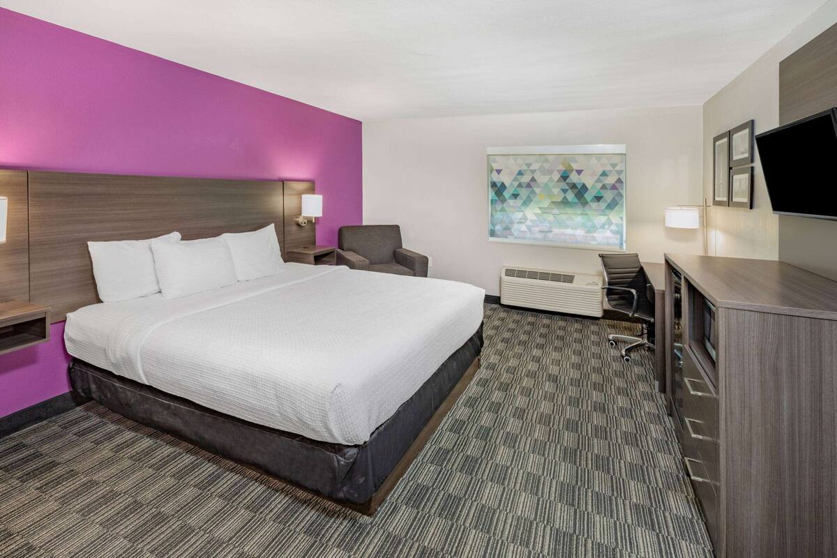 Ein Hotelzimmer mit einem großen Bett, einem Schreibtisch, einem Sessel, einem Fernseher und einem Bild an der Wand.
