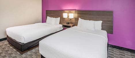 A hotel room with two beds, a nightstand with a lamp, and a purple accent wall.