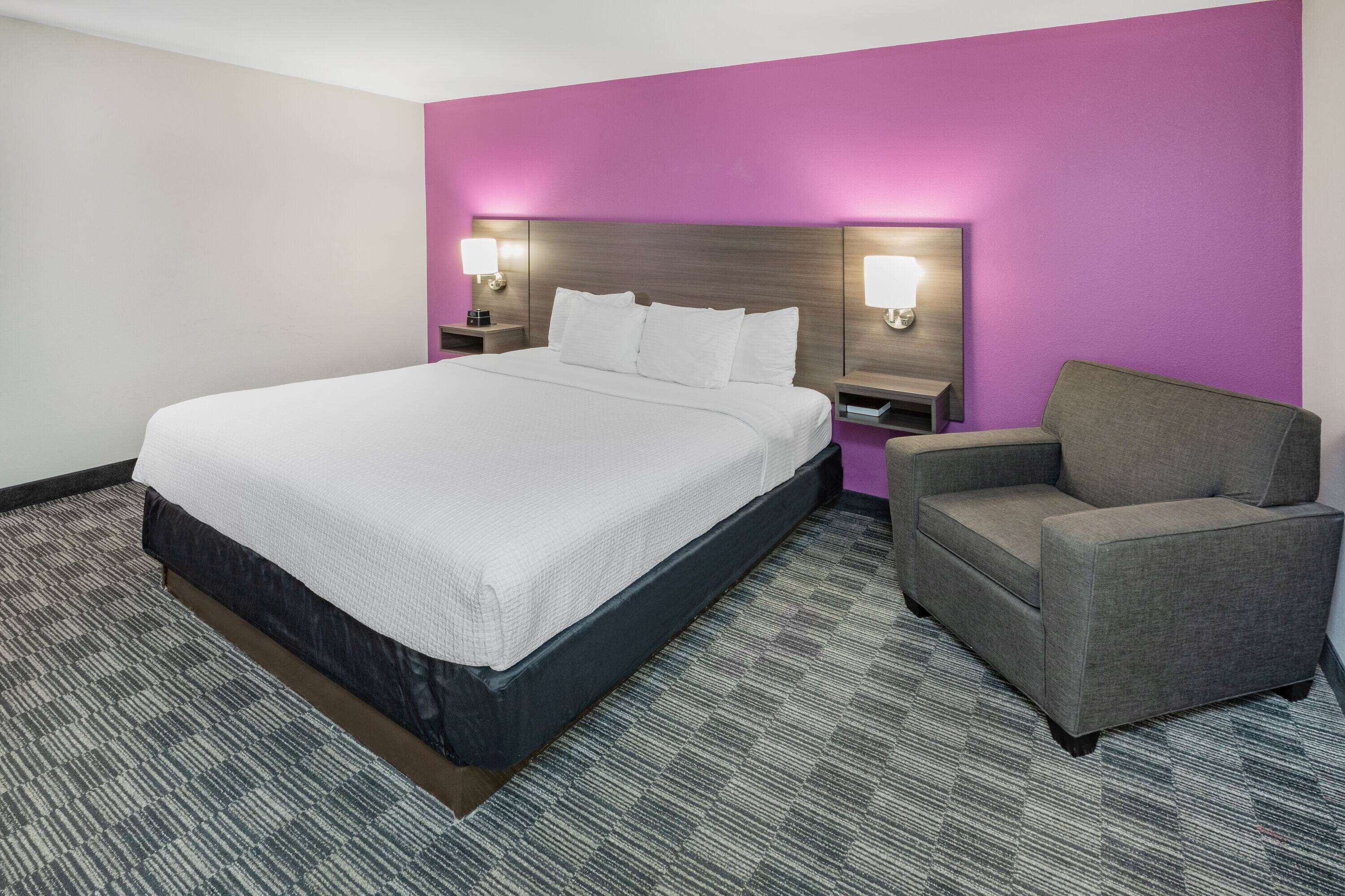 A hotel room with a large bed, a gray armchair, and two bedside lamps.