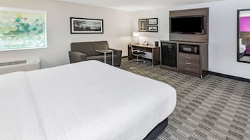 Ein Hotelzimmer mit einem großen Bett, einem Schreibtisch mit Stuhl, einem Fernseher und einer Mikrowelle.