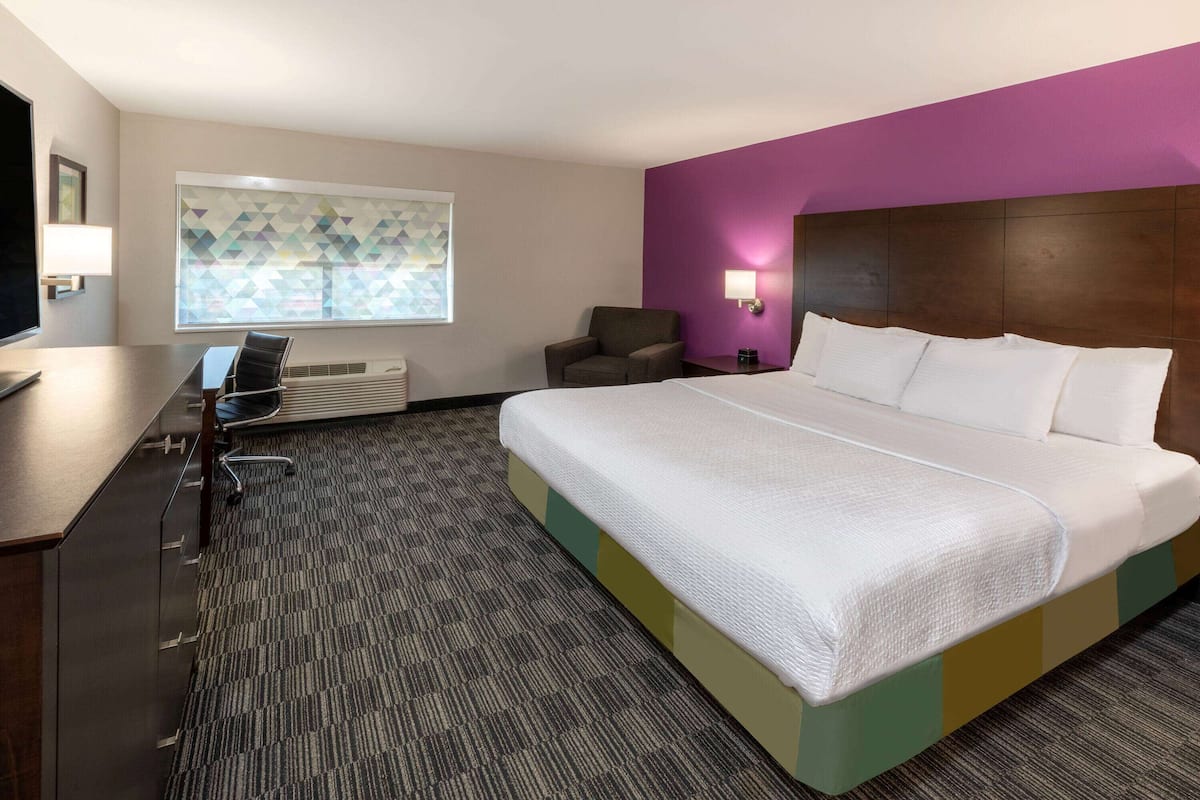 Une chambre d  ’hôtel avec un grand lit, un bureau, une chaise, une télévision et une fenêtre ornée d’un motif géométrique.