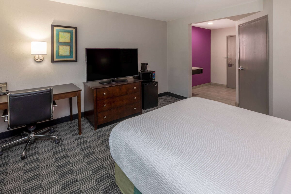 Une chambre d’hôtel comprenant un lit, un bureau avec une chaise, une télévision, une machine à café et une porte donnant sur une autre pièce.