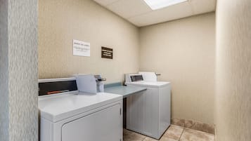 A laundry area with two front-loading washers and dryers, a speed queen commercial dryer, and signs indicating laundry services.