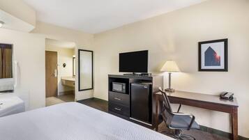 A hotel room with a bed, a desk, a chair, a television, a microwave, a refrigerator, a lamp, and a framed picture on the wall.