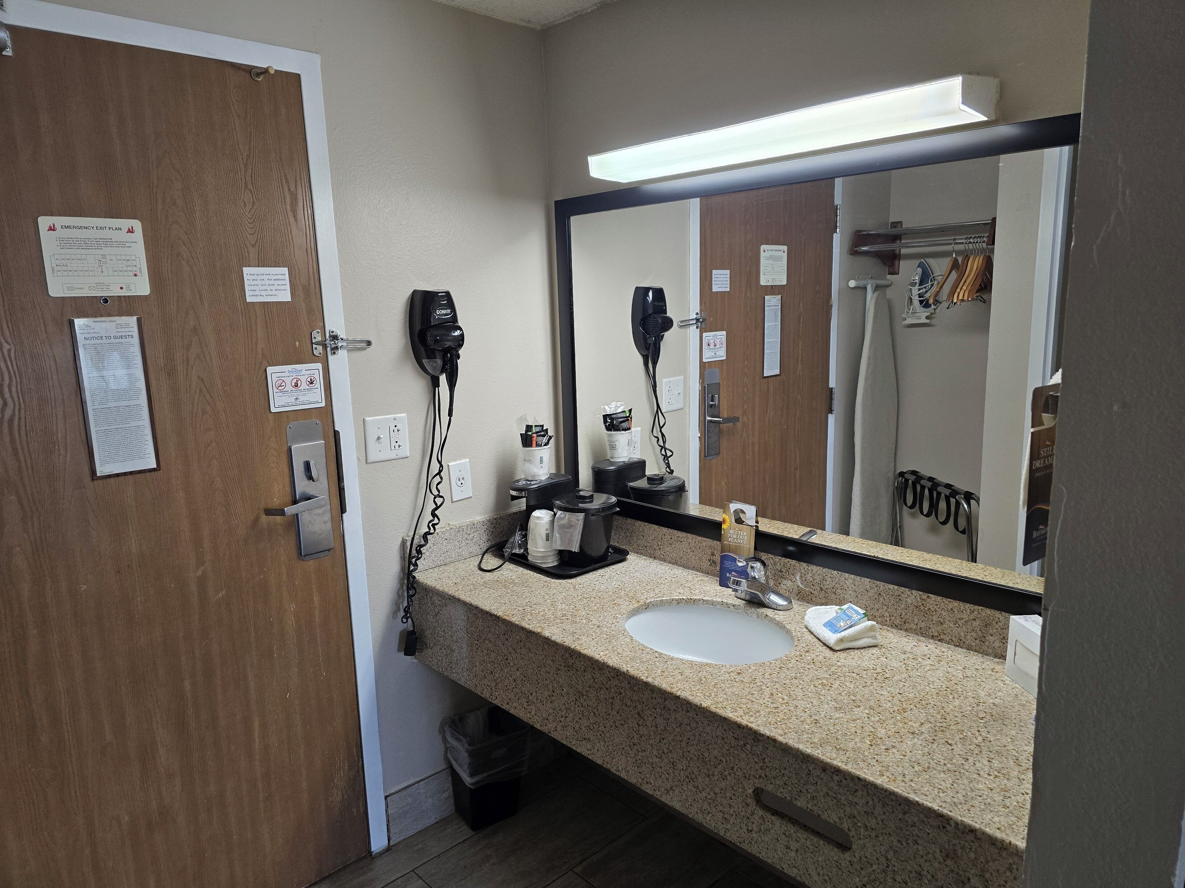 A hotel bathroom with a sink, mirror, hairdryer, and various toiletries.