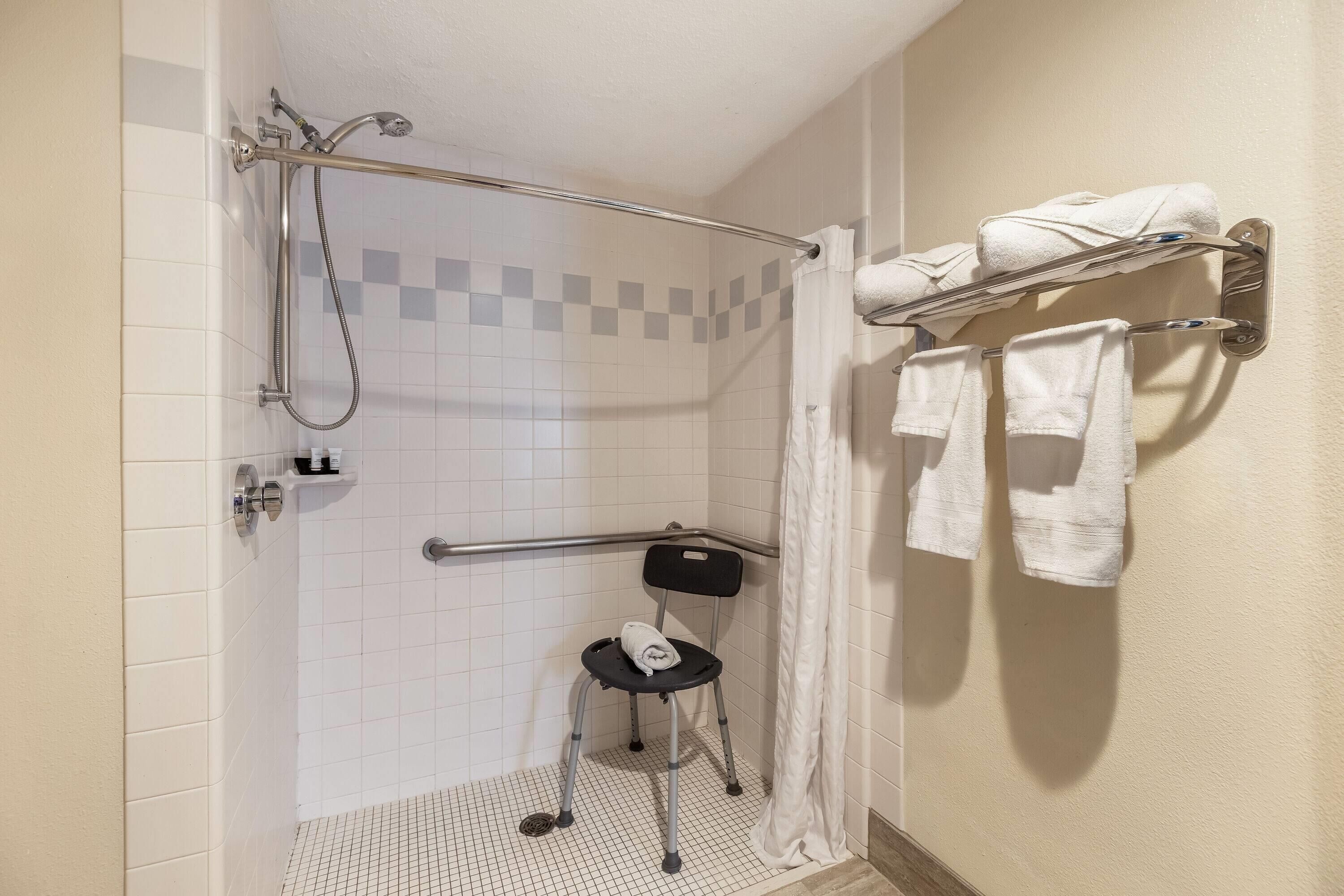Ducha con barra de apoyo, asiento accesible en silla de ruedas y toallero con toallas.