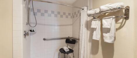 Ducha con barra de apoyo, asiento accesible en silla de ruedas y toallero con toallas.