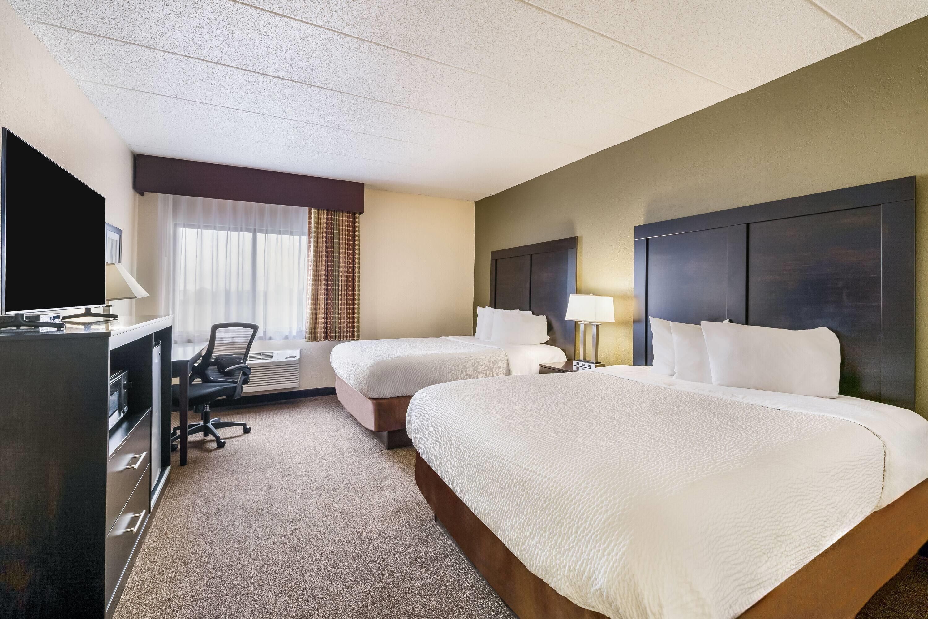 A hotel room with two beds, a desk with a chair, a television, and a window with curtains.