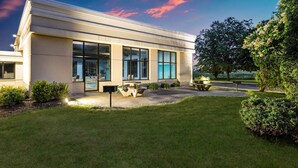 A modern building with large windows, a well-maintained lawn, and outdoor seating. - Baymont by Wyndham Janesville (Janesville)