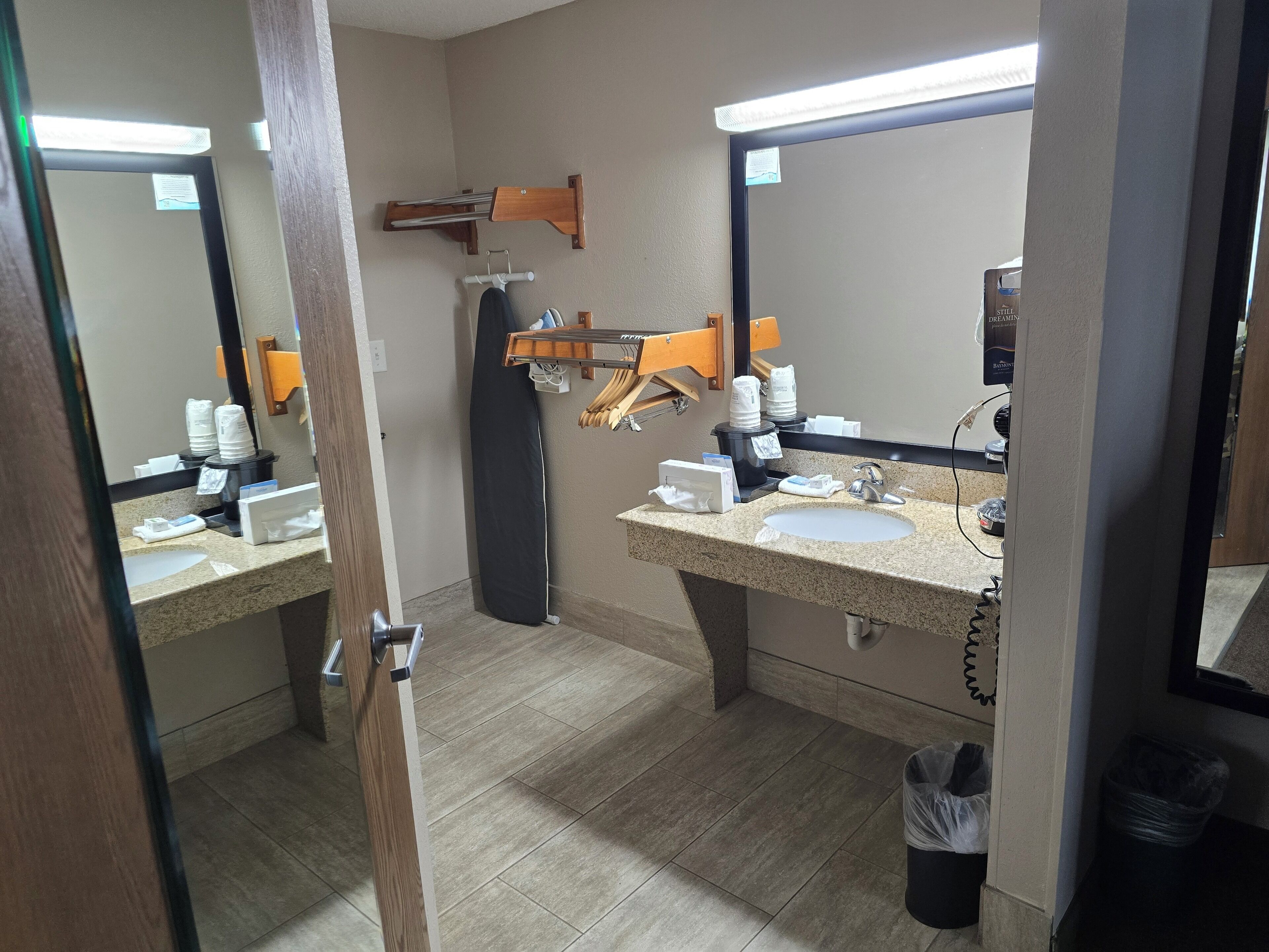 A hotel bathroom with two sinks, a mirror, a towel rack, and a hairdryer.
