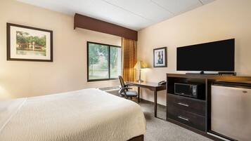 Habitación de hotel con cama, escritorio, televisor y refrigerador.