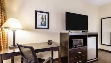 A hotel room with a desk, chair, TV, microwave, refrigerator, and a framed picture on the wall.