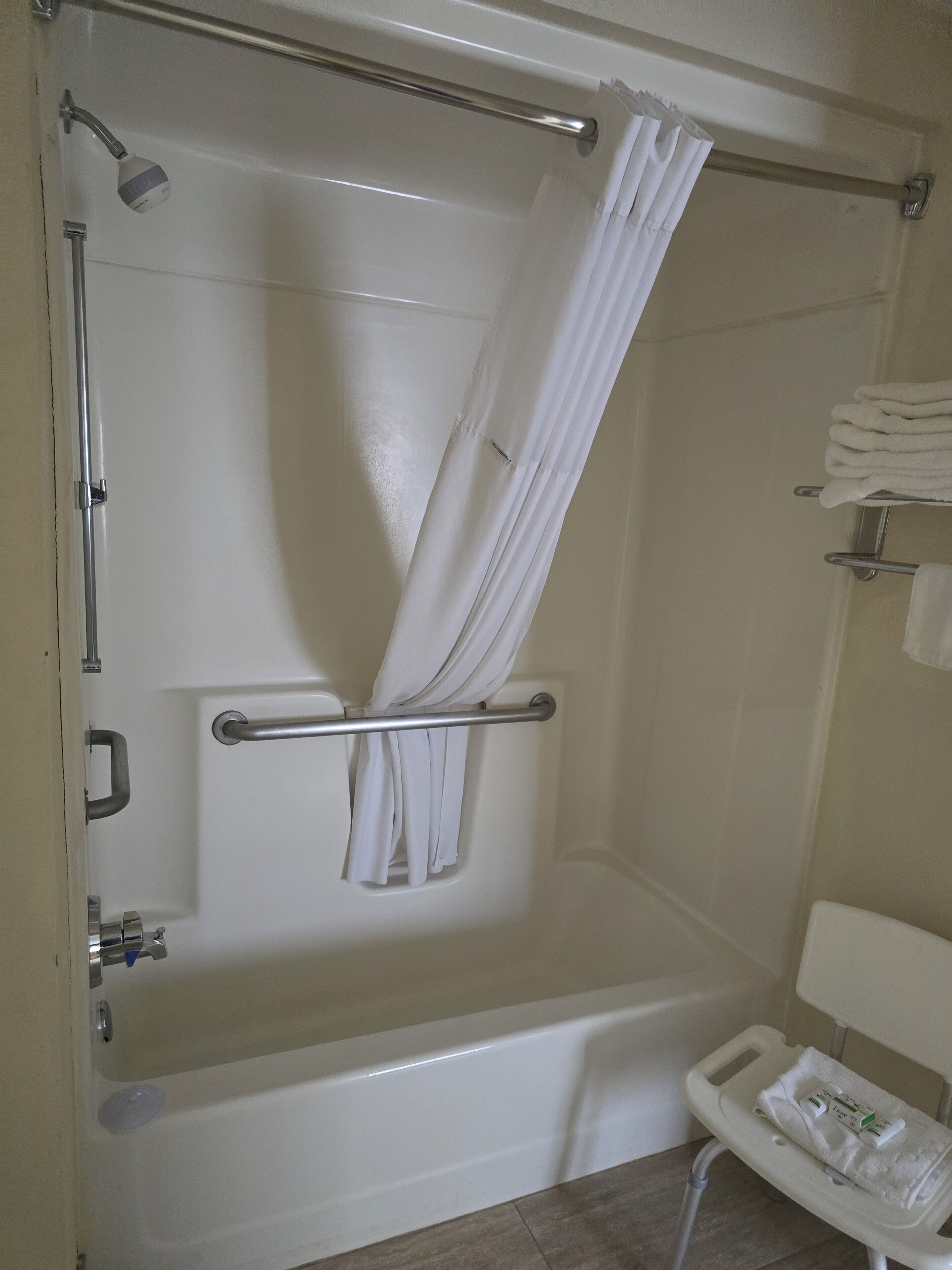 A bathroom with a bathtub, shower curtain, towel rack, and a small stool with towels.