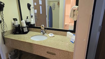 Baño de hotel con encimera de granito, un lavamanos, secador de pelo, plancha y cubo de basura.