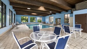 A pool area with chairs and tables, wooden beams on the ceiling, and large windows. - Baymont by Wyndham Janesville (Janesville)