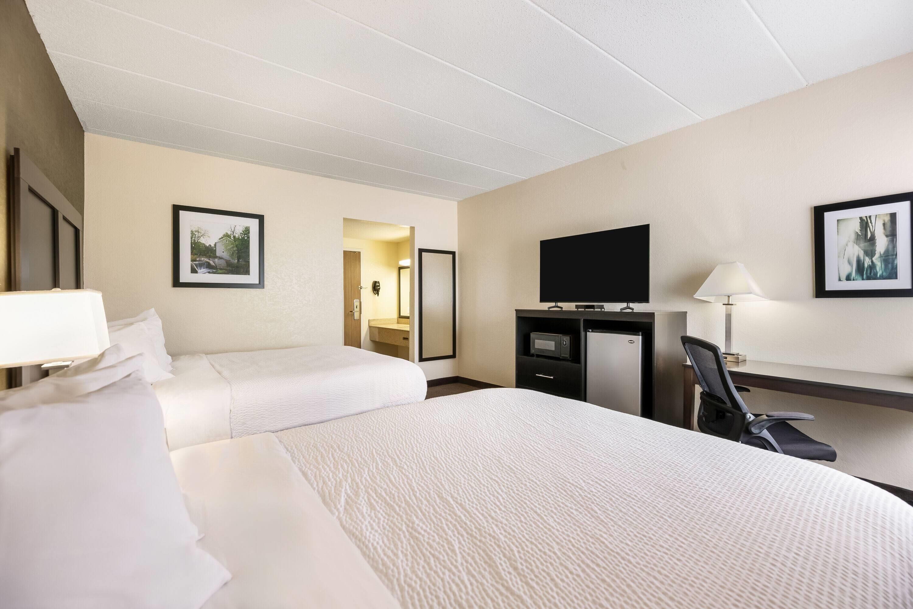 A hotel room with two beds, a desk with a flat-screen TV, a chair, and a desk lamp.