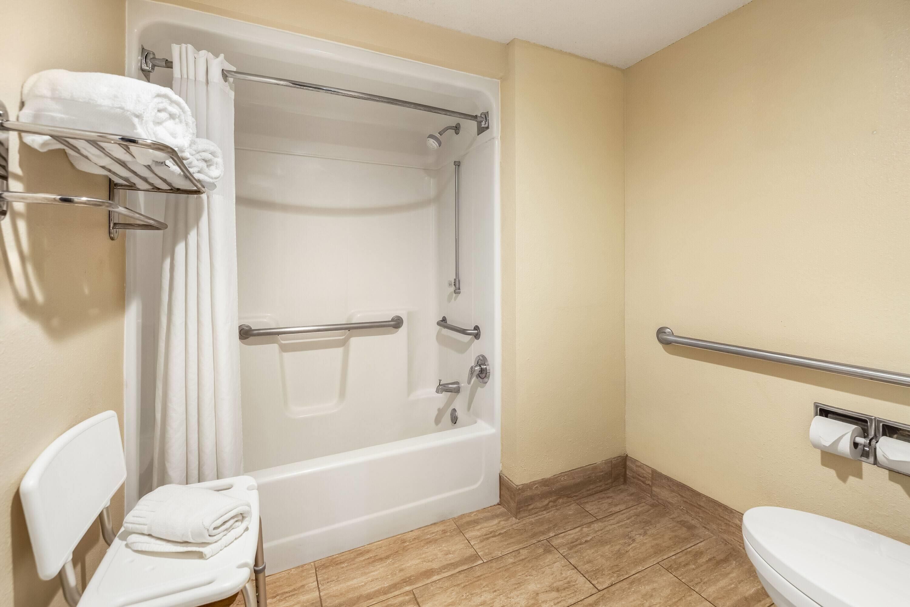 A bathroom with a bathtub, toilet, and handrails.