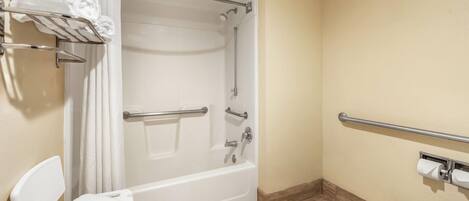 A bathroom with a bathtub, toilet, and handrails.