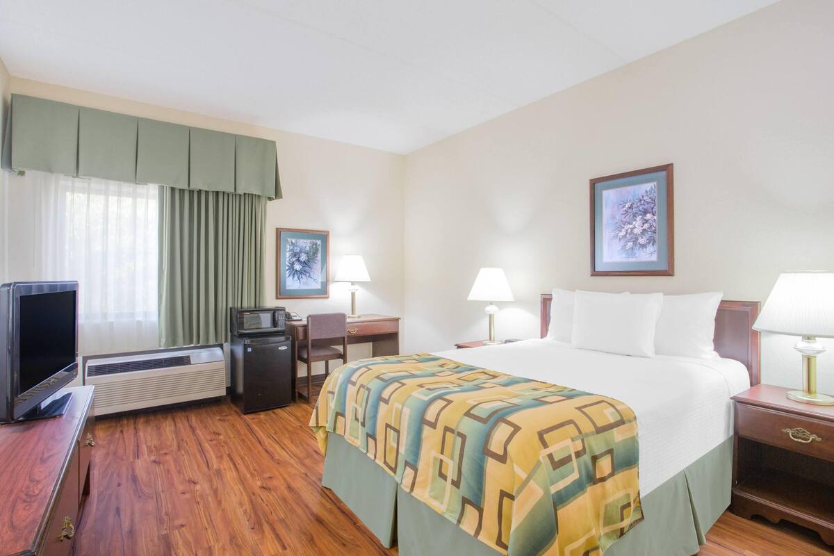 A hotel room with a bed, a desk, a television, a desk lamp, a picture frame, and a window with curtains.
