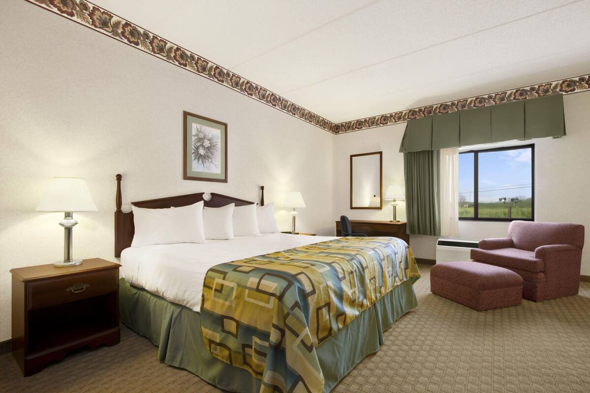 A hotel room with a large bed, two bedside tables with lamps, a chair, and a window with a view of the outdoors.